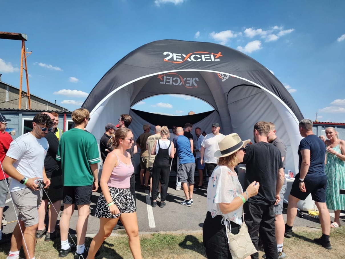 a group of people walking past a black tent and a blue sky with clouds