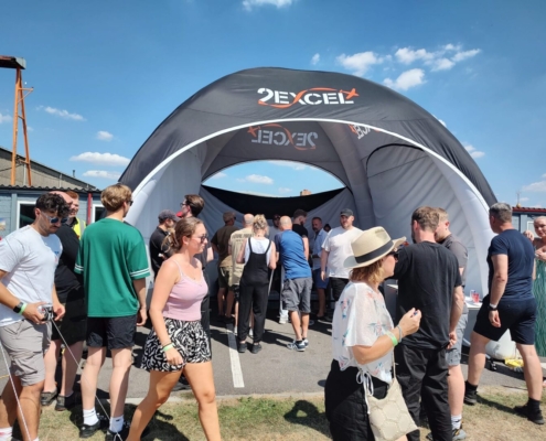 a group of people walking past a black tent and a blue sky with clouds